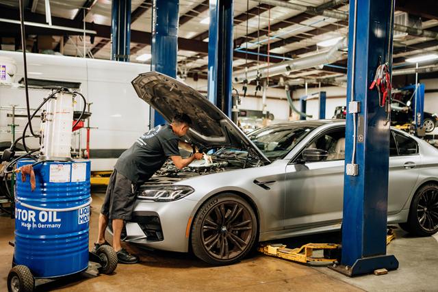 Technician working under the hood of a silver BMW M5 beside a drum of German motor oil