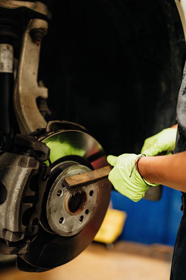 Technician wire-brushing a wheel hub during brake rotor and caliper service