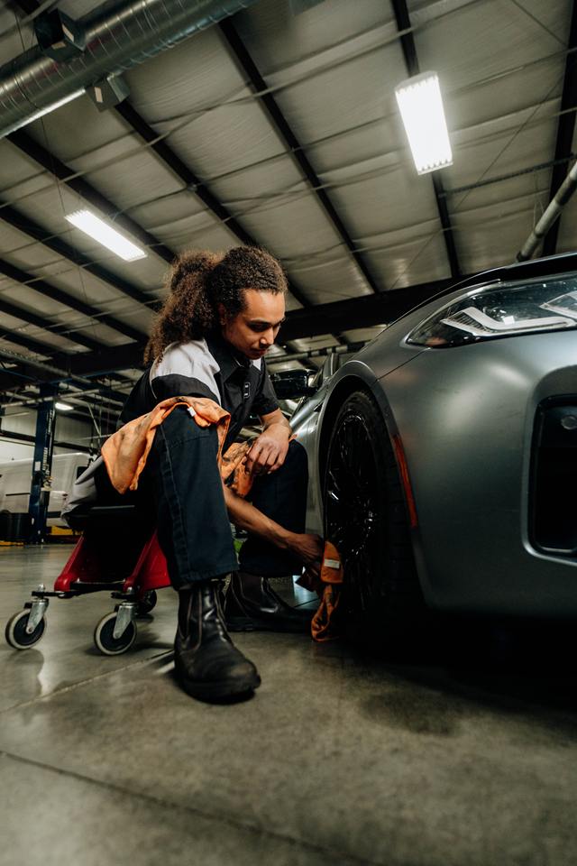 Technician on a shop creeper wiping down the wheel of a gray car
