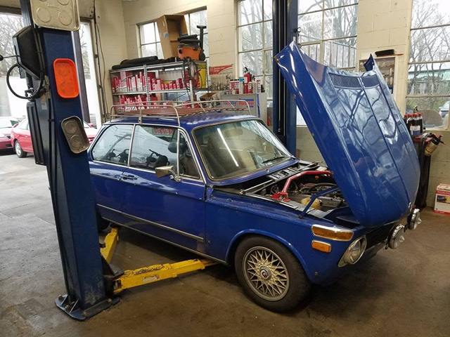 Classic blue BMW with a roof rack and its hood open beside a lift
