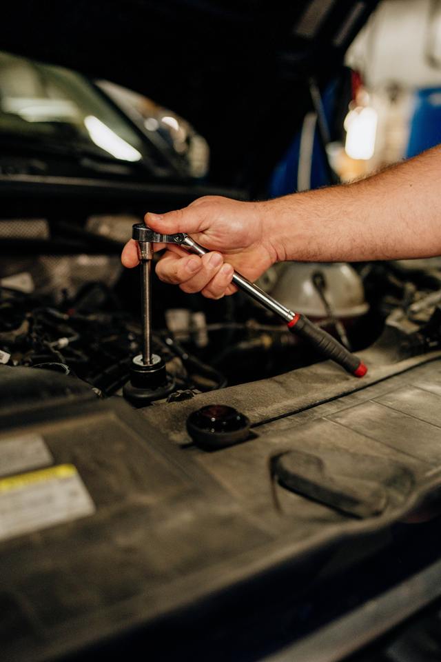 Technician tightening a fitting in an engine bay with a ratchet