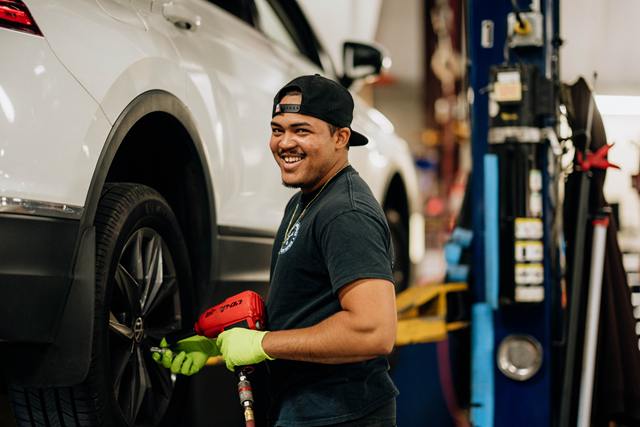 Technician using an impact wrench on the wheel of a white SUV