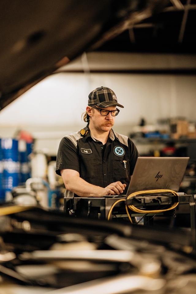 Technician running vehicle diagnostics on a laptop beside an open hood