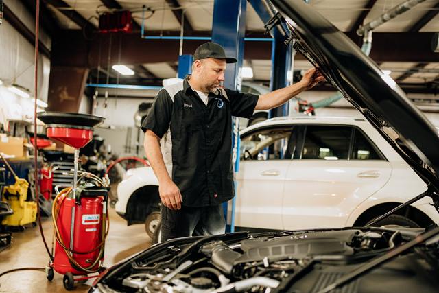 Technician checking under the hood beside an oil drain, with a white SUV in the next bay