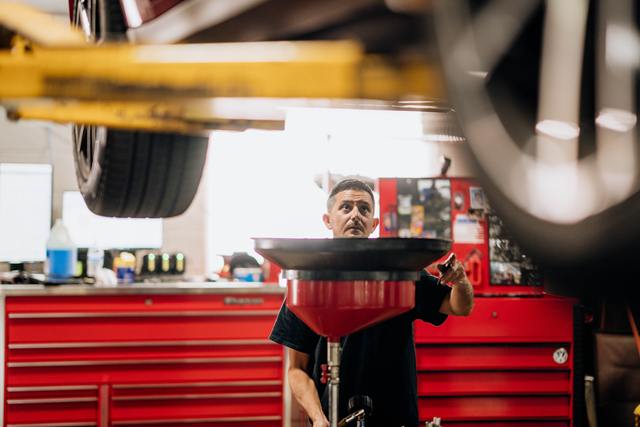 Technician positioning an oil drain under a car on the lift
