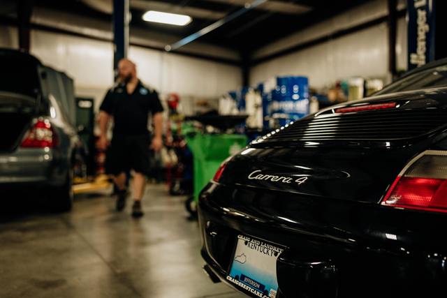 Black Porsche 911 Carrera 4 in the shop as a technician walks past
