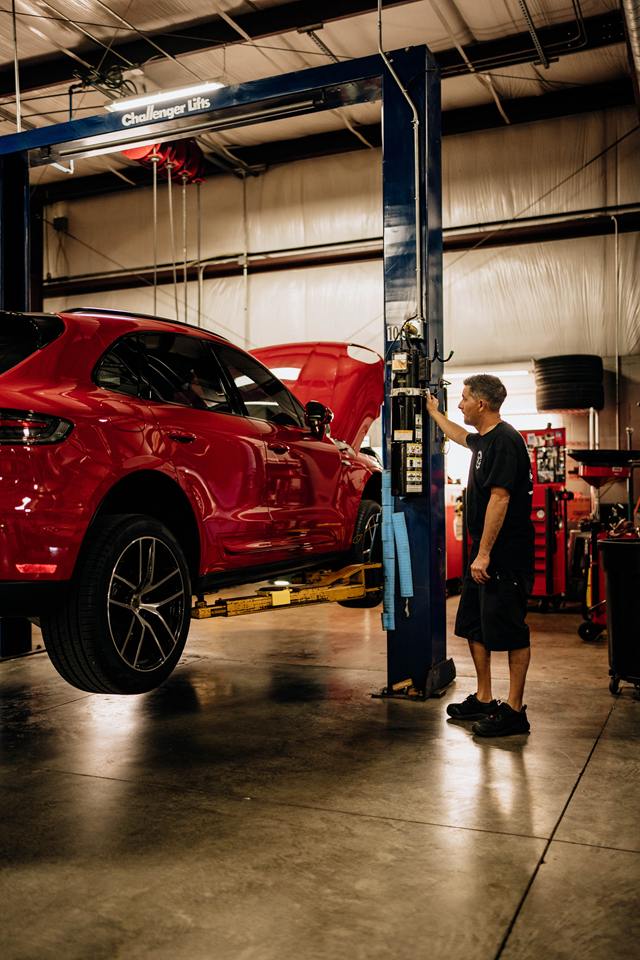 Technician raising a red Porsche Macan on a two-post lift