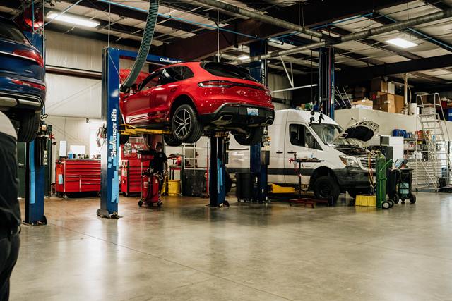 Red Porsche Macan raised on a lift, with a white Mercedes-Benz Sprinter van in the next bay
