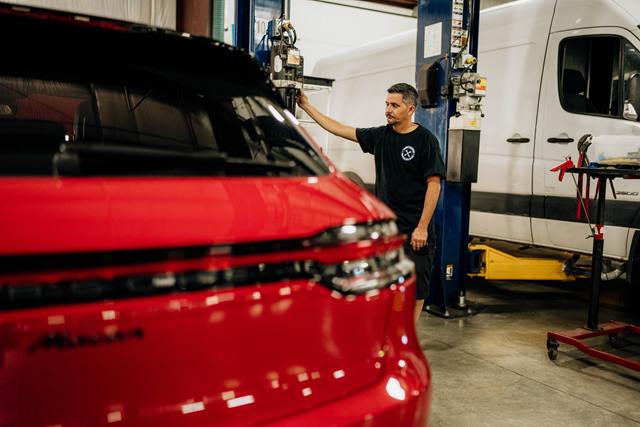Technician operating the lift controls beside a red Porsche Macan