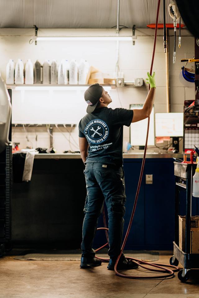 Technician in a Turning Wrenches European Auto Repair shirt pulling down an air hose at the workbench