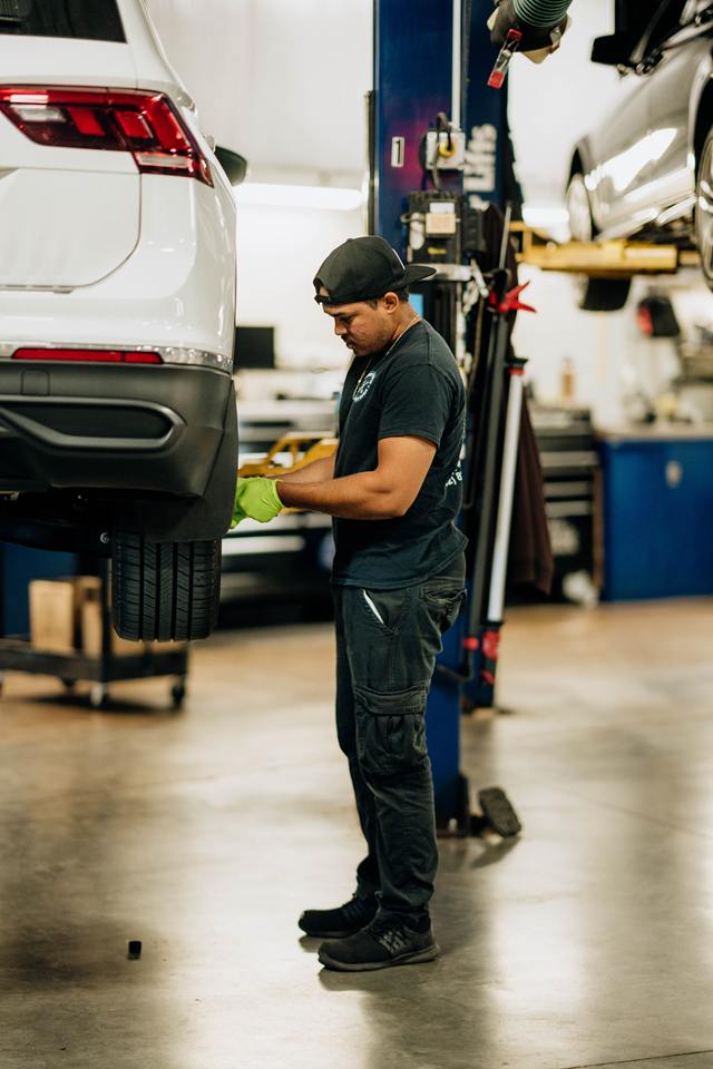 Technician in work gloves beside a white SUV raised on a lift