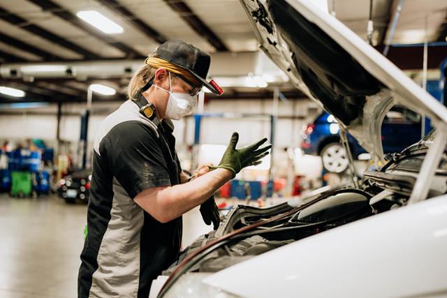 Technician pulling on work gloves before working under the hood of a white vehicle