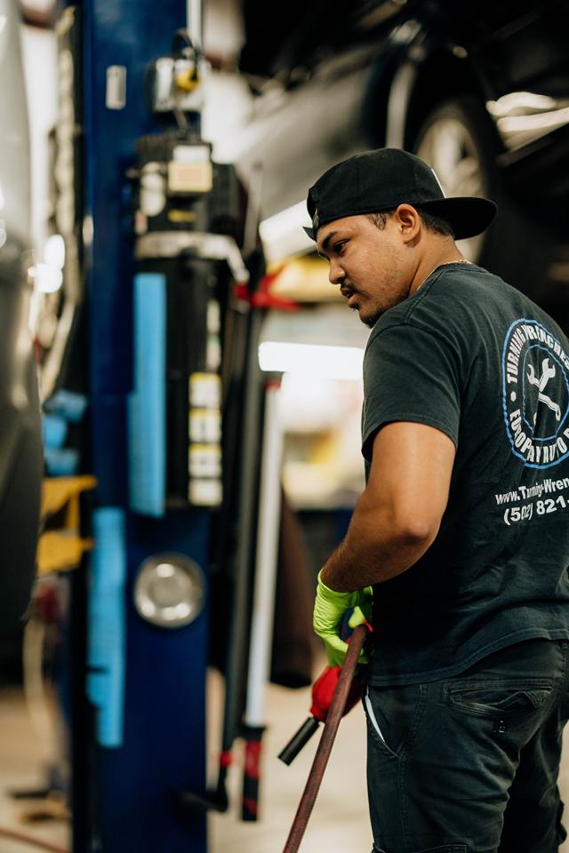 Technician in a Turning Wrenches shirt pulling an air hose beside a lift