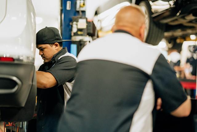 Two technicians working at the rear of a white SUV on a lift