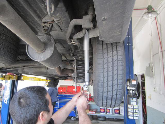 Technician installing a rear shock absorber on a vehicle raised on a lift