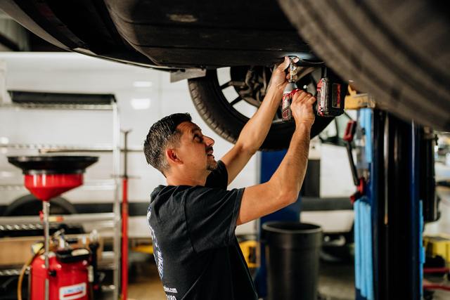 Technician using a cordless impact tool under a vehicle on the lift