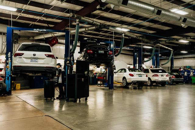 White Volkswagen Tiguan and a black Mercedes-Benz sedan on lifts, with a white Mercedes-Benz C-Class and SUV in the bays