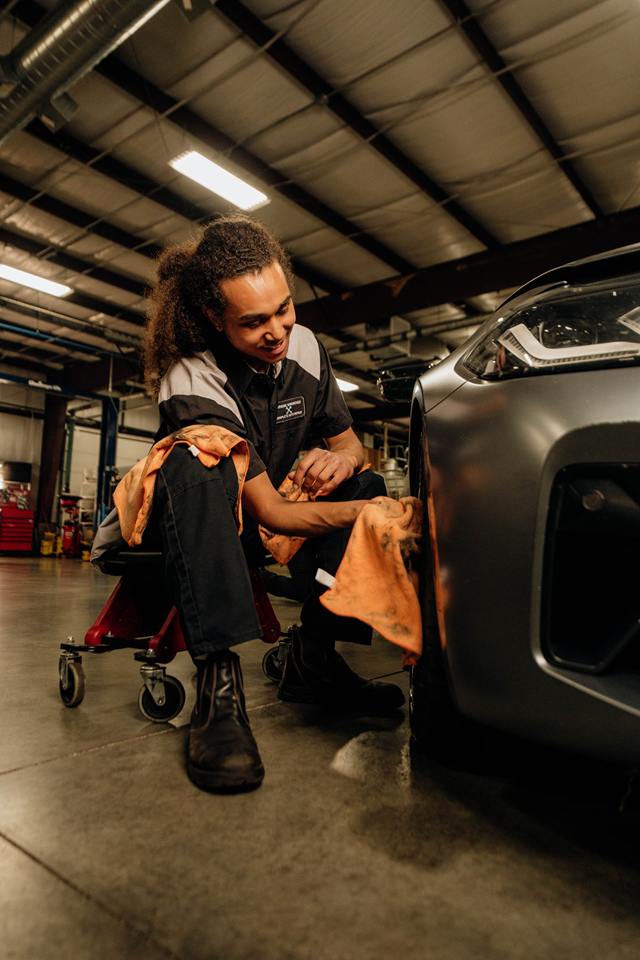 Technician on a creeper cleaning the wheel of a gray car