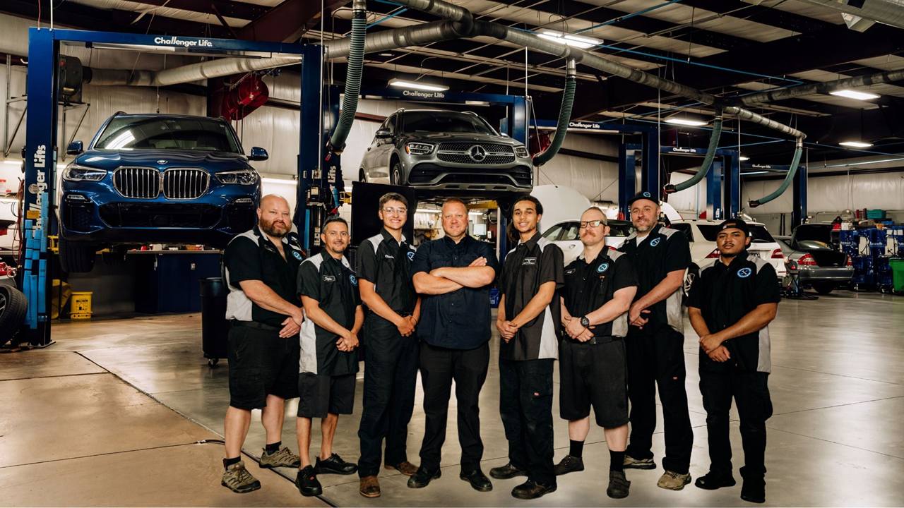 The Turning Wrenches European Auto Repair team in the Louisville shop, with a blue BMW SUV and a gray Mercedes-Benz SUV on lifts behind them